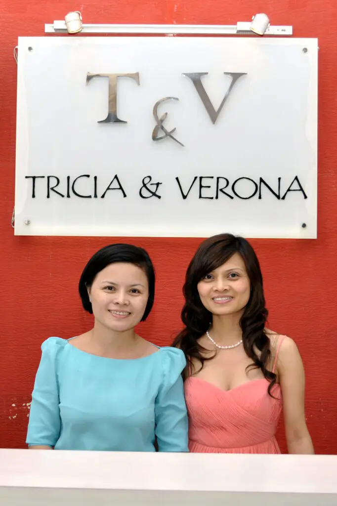 Two women posing in front of a sign reading T & V Tricia & Verona.